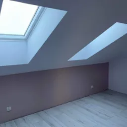 Poddasze po remoncie z dwoma oknami dachowymi, ściana pomalowana na dwa kolory: beżowy i biały, podłoga wyłożona panelami imitującymi drewno.