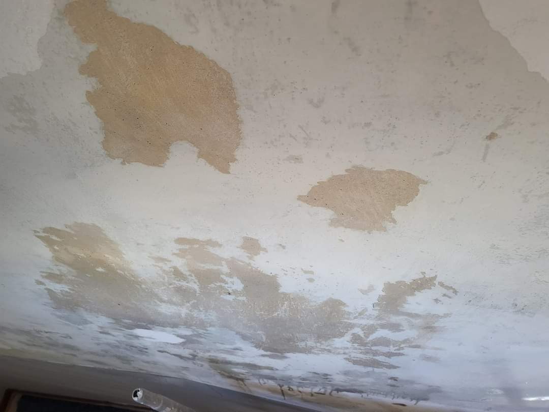 Nierówna powierzchnia sufitu z widocznymi plamami po szpachlowaniu i śladami wilgoci, ukazująca przygotowanie do dalszych prac wykończeniowych.