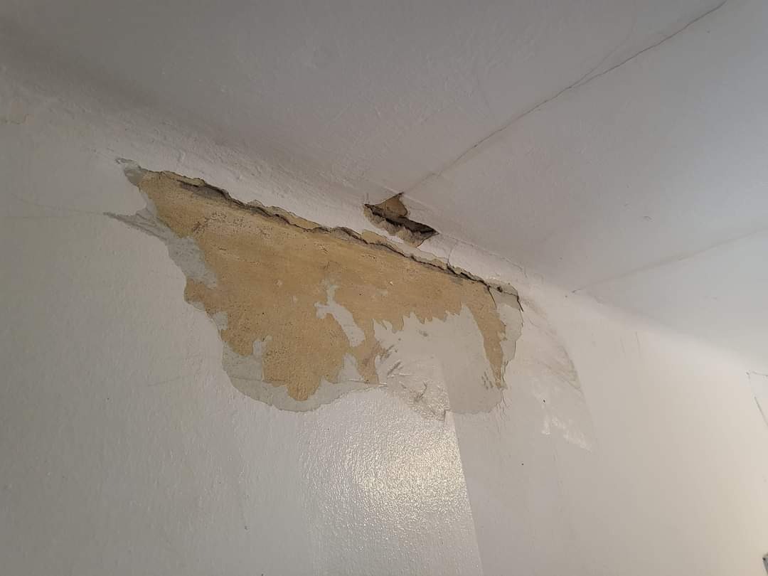 Uszkodzony fragment ściany i sufitu z odpadającym tynkiem, widoczne pęknięcia i warstwy farby, przygotowanie do naprawy.