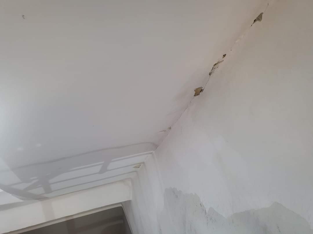 Niedoskonałości na styku ściany i sufitu, widoczne pęknięcia i ubytki w białej farbie, przygotowanie do prac wykończeniowych.