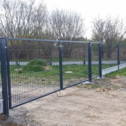 Nowa brama wjazdowa z paneli stalowych, zamontowana na betonowej podmur&oacute;wce, widok z zewnątrz posesji, z boku stoi mężczyzna.