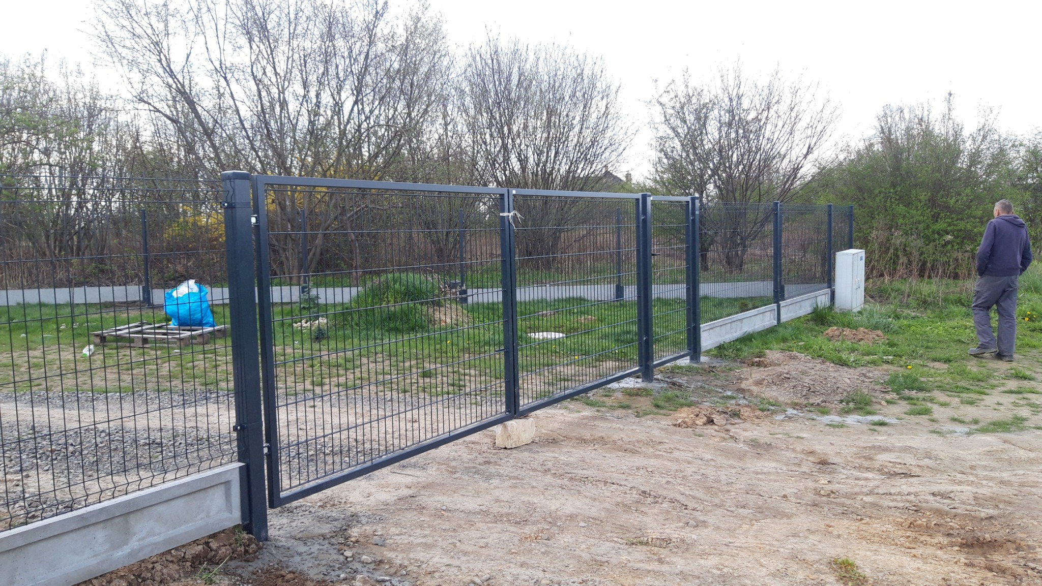 Nowa brama wjazdowa z paneli stalowych, zamontowana na betonowej podmurówce, widok z zewnątrz posesji, z boku stoi mężczyzna.
