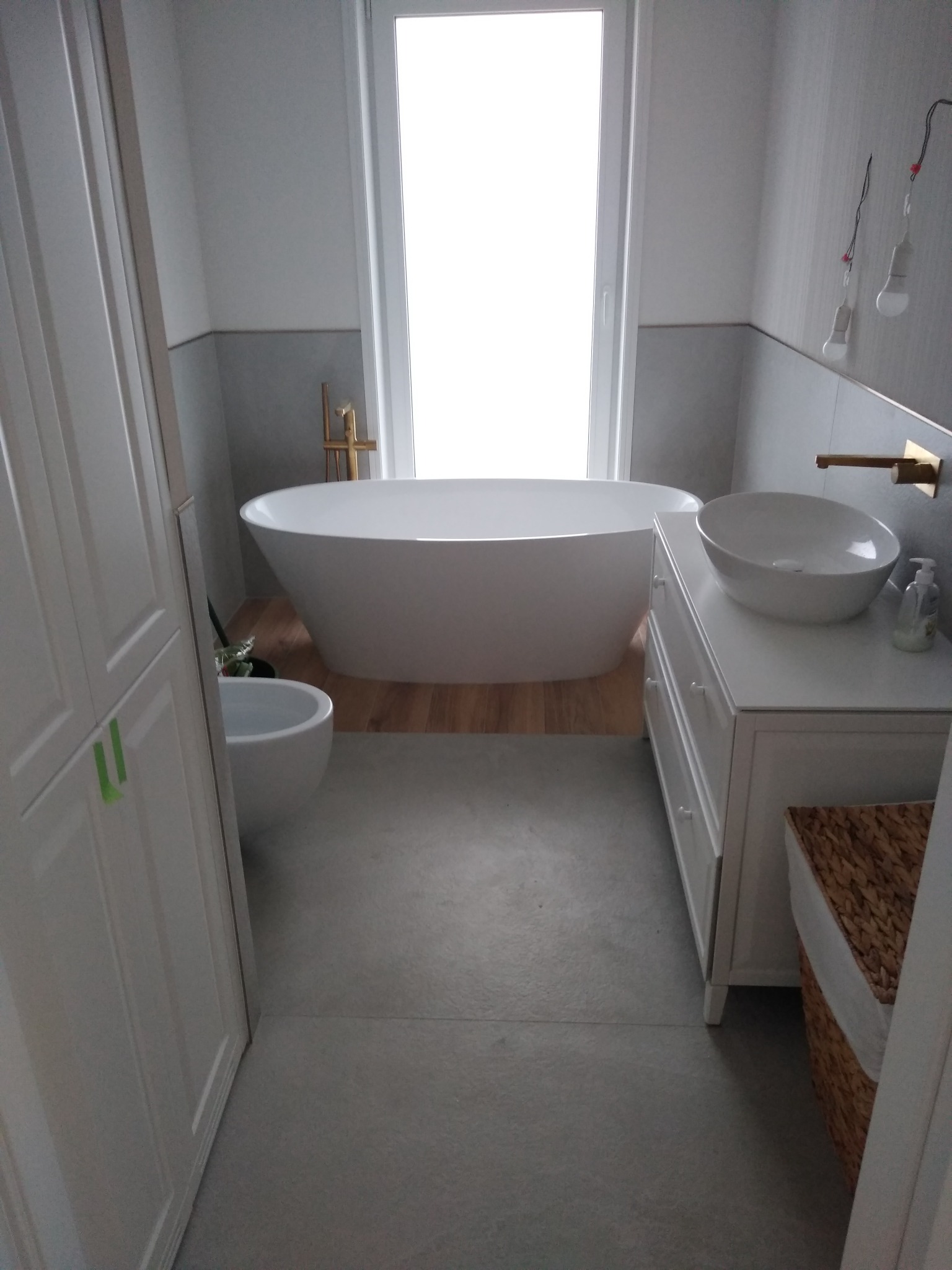 Nowoczesna łazienka w odcieniach bieli i szarości z wolnostojącą wanną, bidetem, umywalką nablatową na komodzie i drewnopodobną podłogą w strefie wanny.