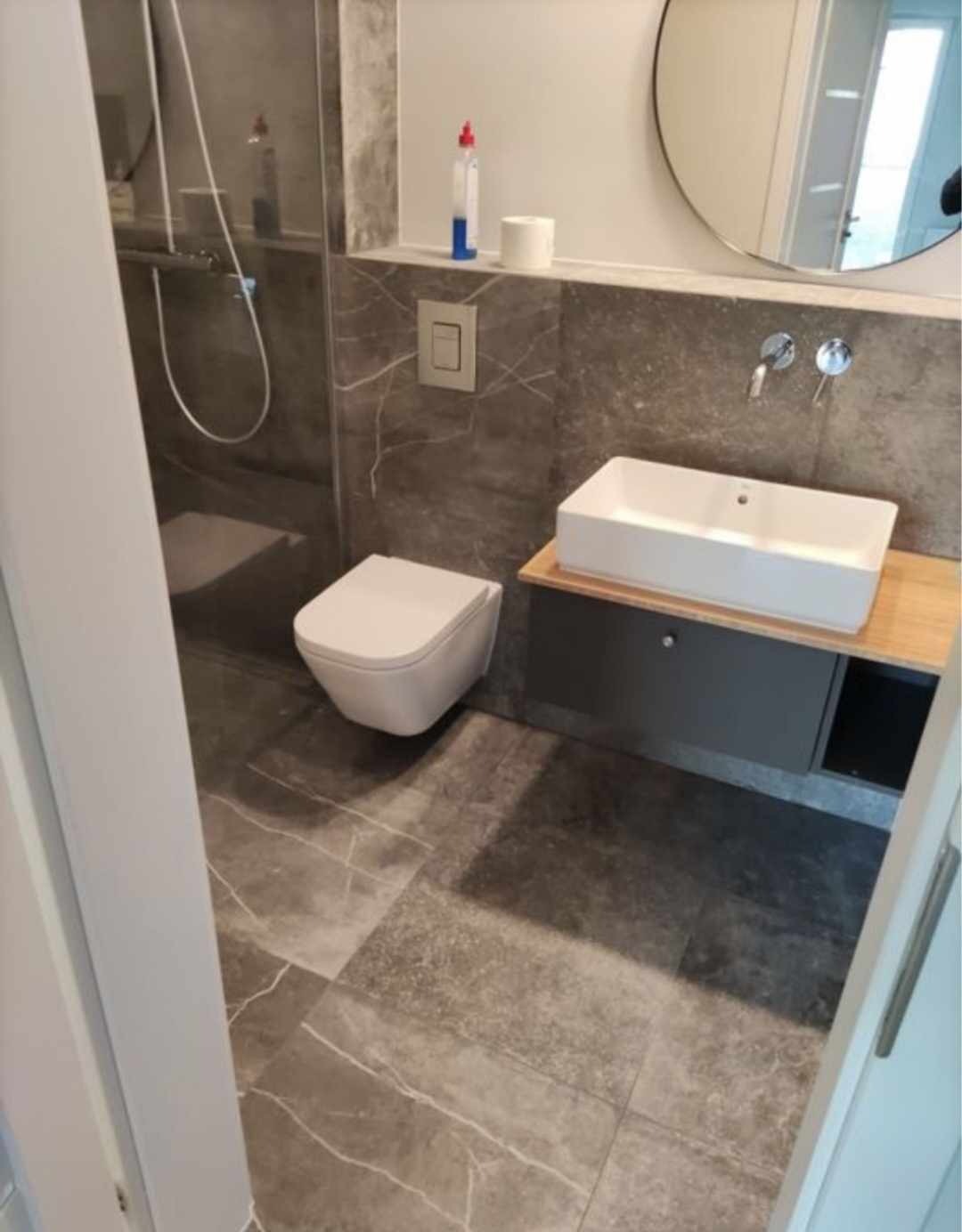 Nowoczesna łazienka z szarymi płytkami imitującymi marmur, wiszącą toaletą i prostokątną umywalką nablatową.