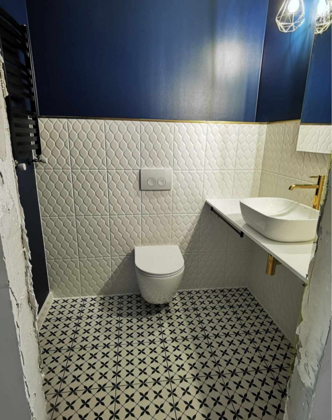 Nowoczesna łazienka z białą ceramiką, wzorzystą podłogą i granatową ścianą, wykończona złotymi akcentami