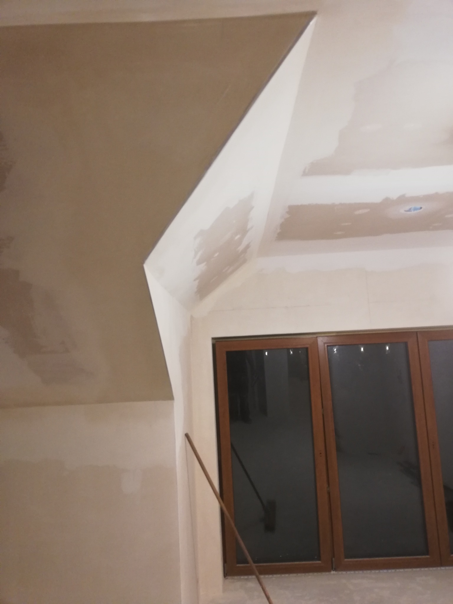 Poddasze w trakcie prac wykończeniowych: ściany i sufit częściowo pokryte gładzią, widoczne drewniane okno balkonowe, na podłodze mop.