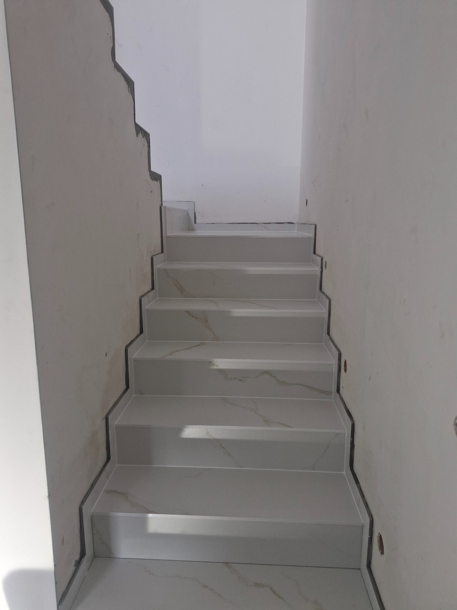 Wyłożone marmuropodobnymi płytkami schody w trakcie wykańczania, widoczne fugi i niedomalowane ściany.
