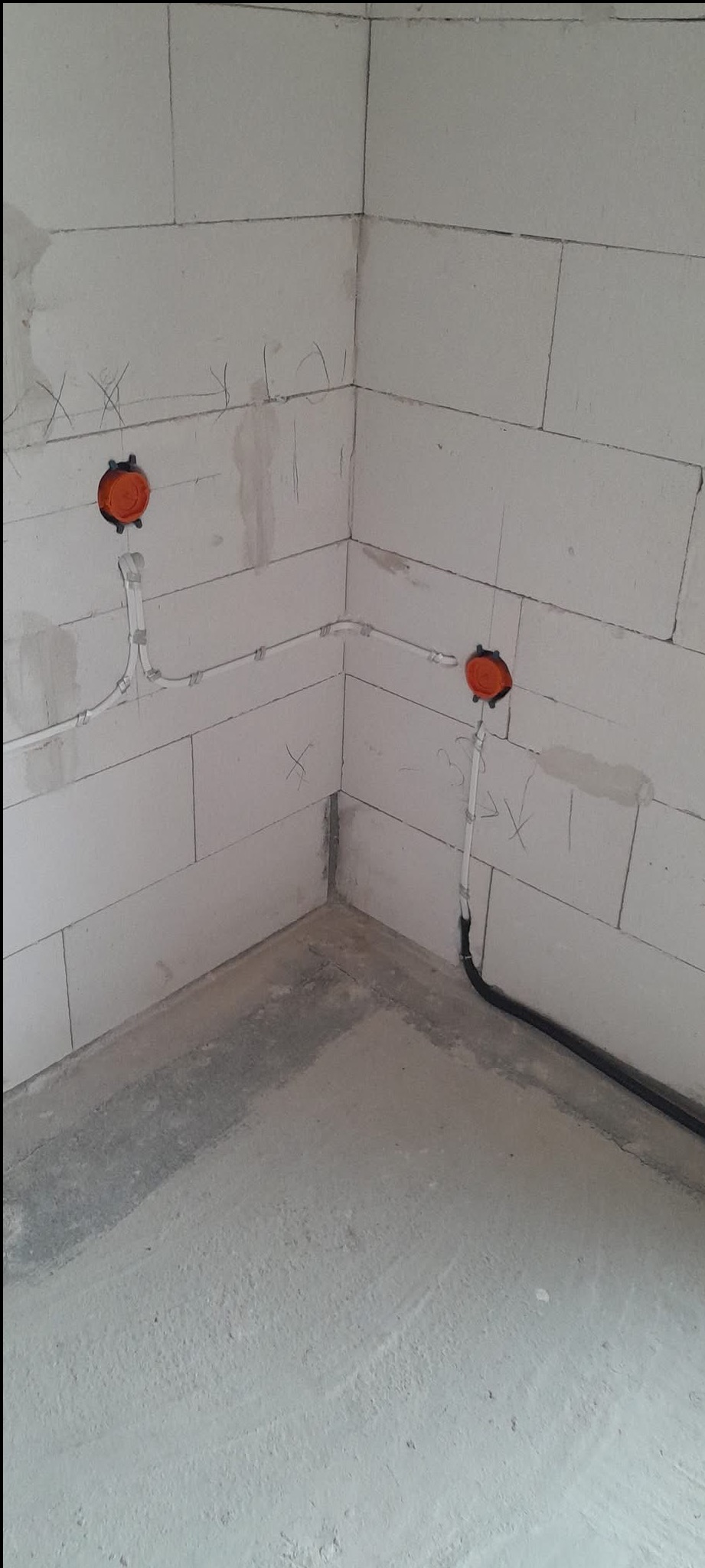 Surowy kąt pomieszczenia z instalacją elektryczną: puszki i kable w ścianie z betonu komórkowego, szara posadzka.