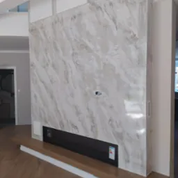 Ściana z dekoracyjną gładzią imitującą marmur, z wbudowanym czarnym biokominkiem i drewnianą półką, widoczna instalacja elektryczna.