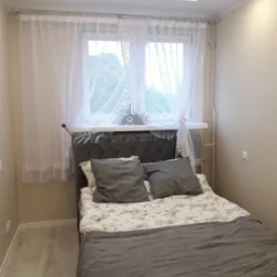 Jasna sypialnia w Sandomierzu po remoncie, z łóżkiem z szarym wezgłowiem, panelami podłogowymi i sufitem podwieszanym z oświetleniem LED.