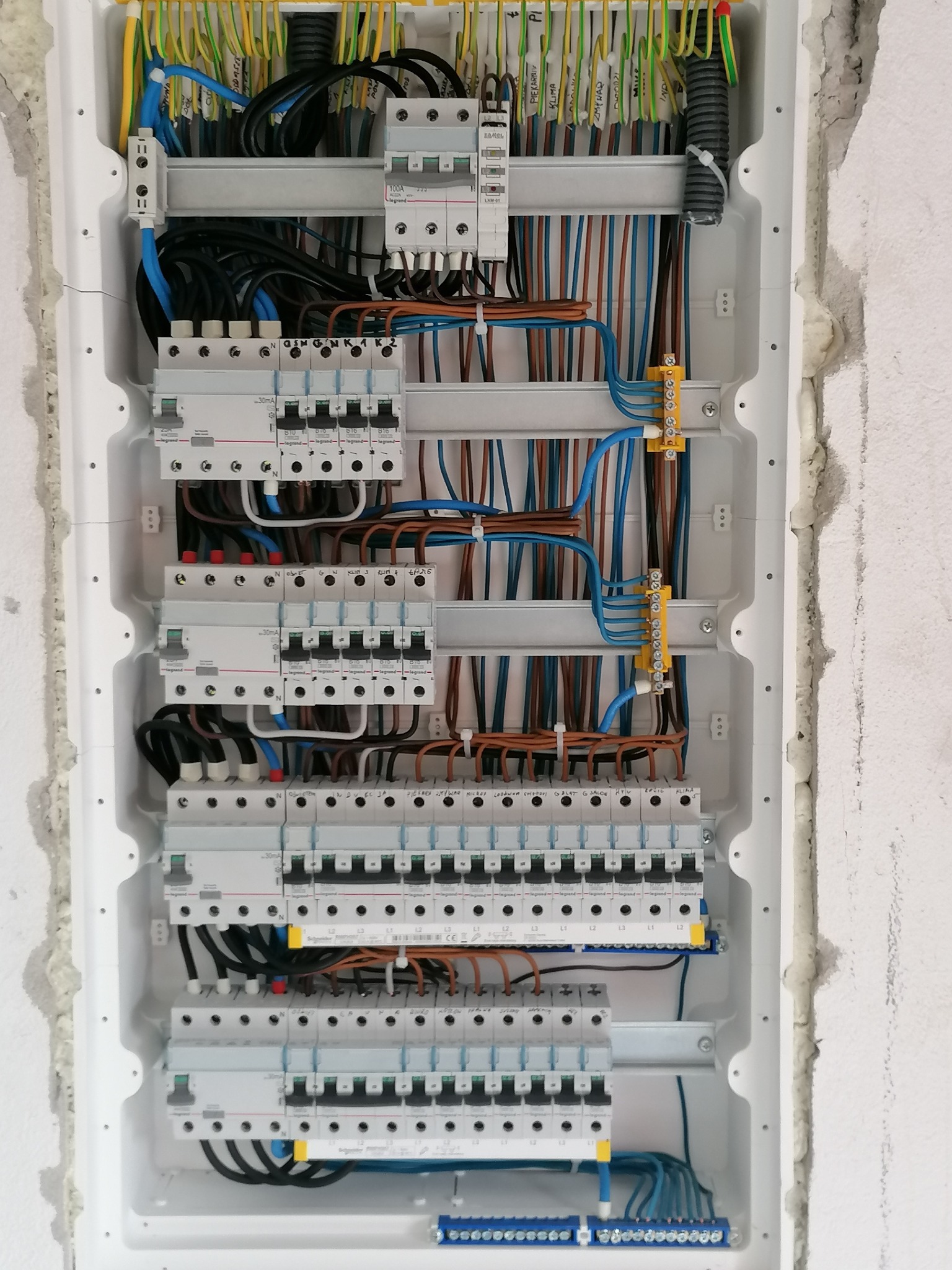 Rozdzielnica elektryczna z zainstalowanymi bezpiecznikami i okablowaniem, widoczna na tle surowej ściany z widoczną pianką montażową.