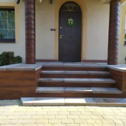 Wejście do domu z brązowymi drzwiami, zdobionymi wieńcem, oraz schodami wykończonymi płytkami imitującymi drewno i szarym kamieniem, z kolumnami o podobnym wykończeniu.