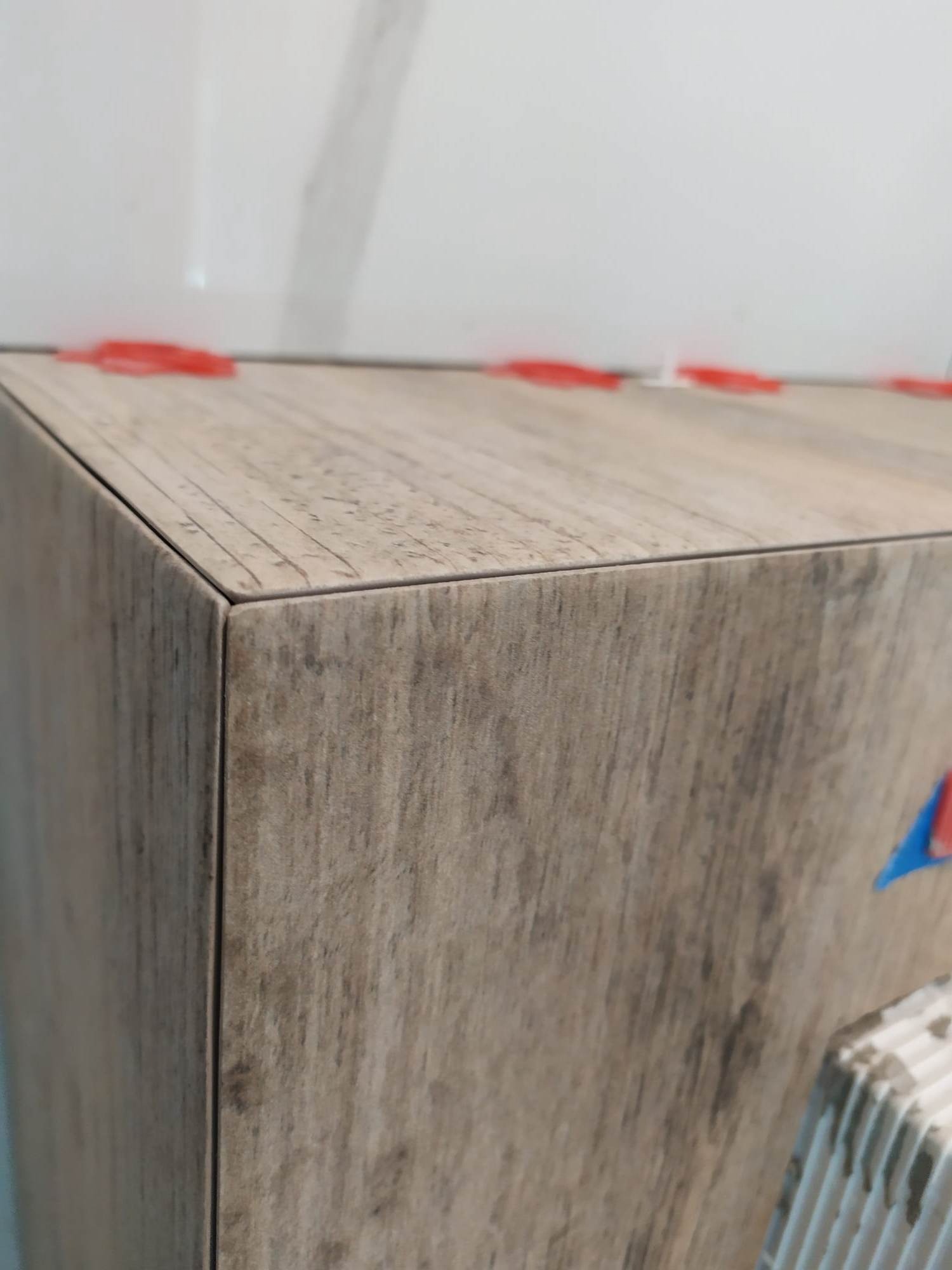 Fragment obudowy z płytek imitujących drewno, z widocznymi czerwonymi klinami poziomującymi i fragmentem grzejnika. Układanie płytek w trakcie realizacji.