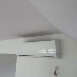 IgloWent - Biały klimatyzator marki Konsi zamontowany na białej ścianie pod skosem dachu, z widocznymi przewodami instalacyjnymi, sugerujący montaż w trakcie wykończenia wnętrza.