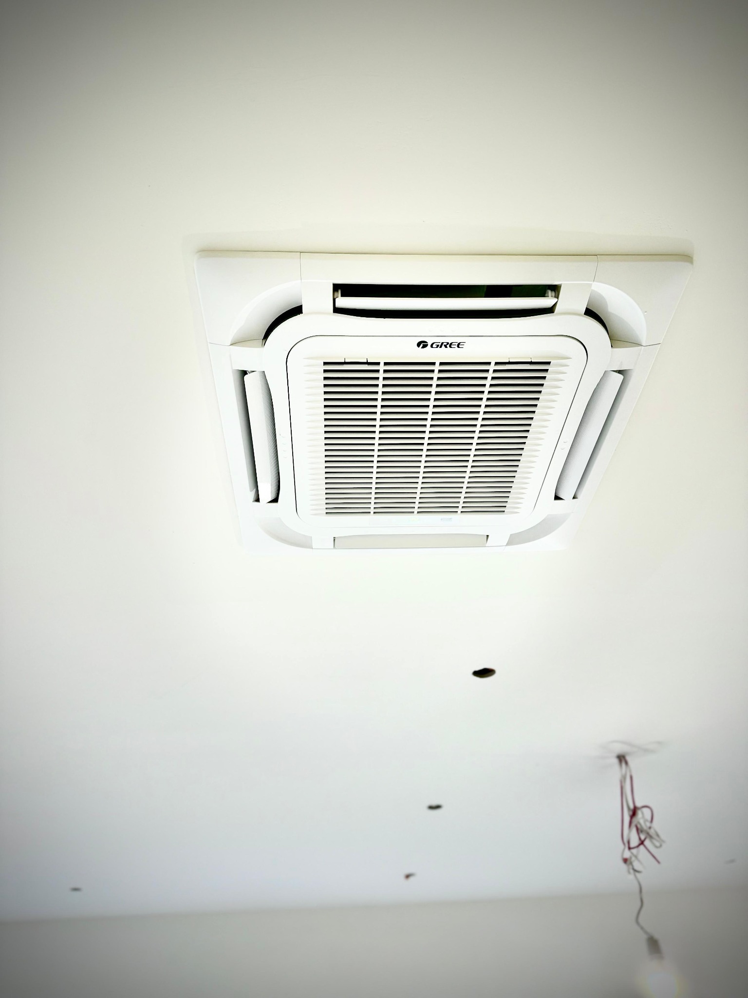 Klimatyzator kasetonowy marki Gree zamontowany w suficie podwieszanym, widoczne niedokończone prace instalacyjne w postaci wystających przewodów.