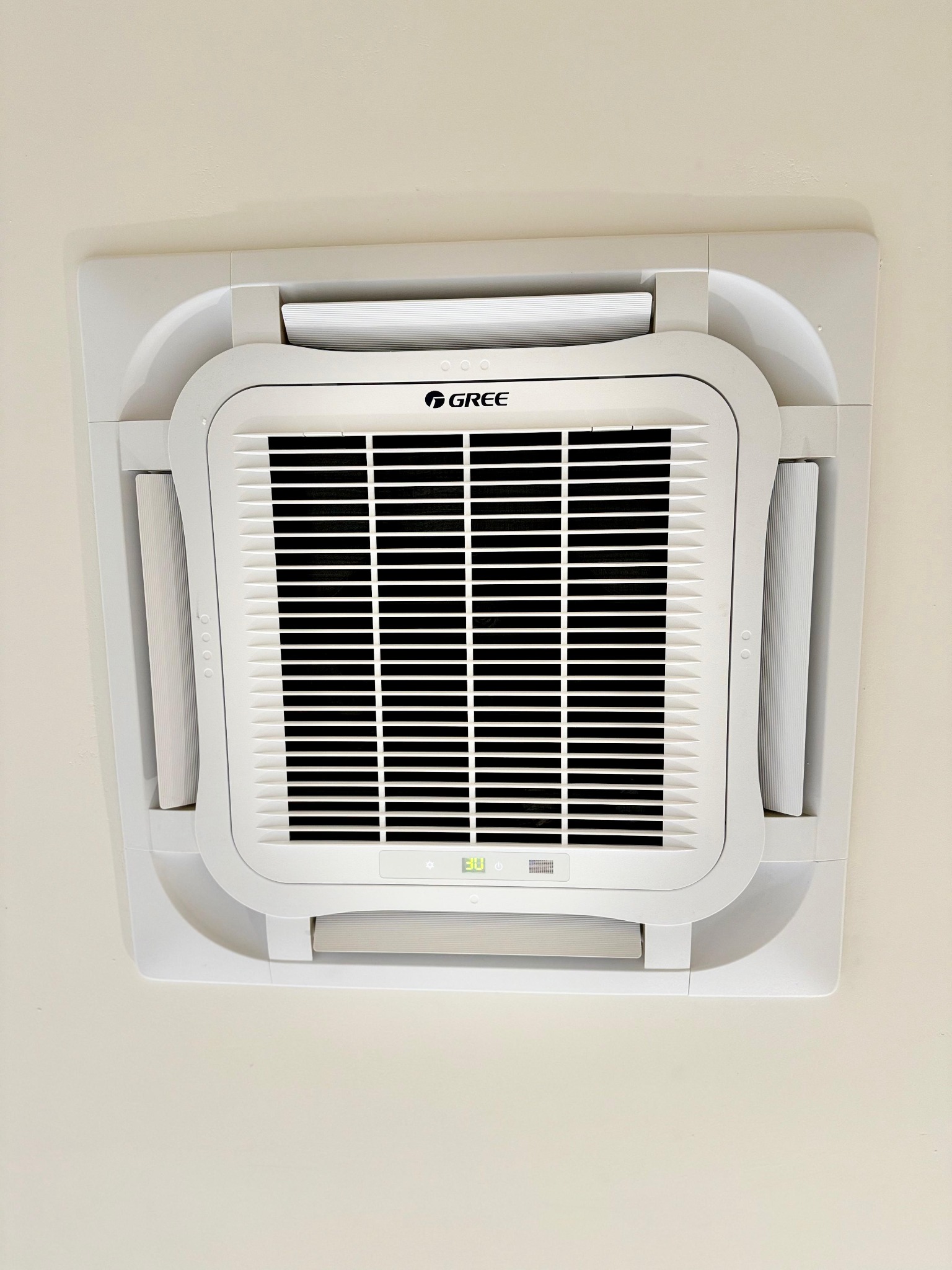 Kasetonowa jednostka klimatyzacyjna marki Gree zamontowana w suficie podwieszanym, widok od dołu, z widocznym wyświetlaczem ustawionej temperatury.