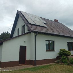 ABC Docieplenia - Dom jednorodzinny z nową, białą elewacją i panelami słonecznymi na brązowym dachu z dachówki, widok z dołu w pochmurny dzień.