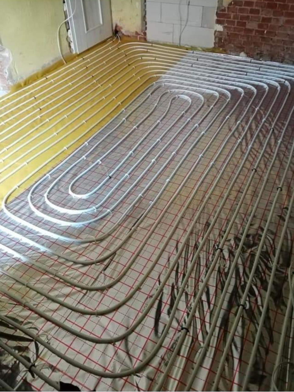 Montaż ogrzewania podłogowego z rur na folii termoizolacyjnej z siatką, widoczne fragmenty ściany w trakcie remontu.