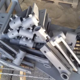 Stalowe elementy konstrukcyjne, rury i płaskowniki po piaskowaniu, leżące na metalowej siatce i drewnianej palecie.