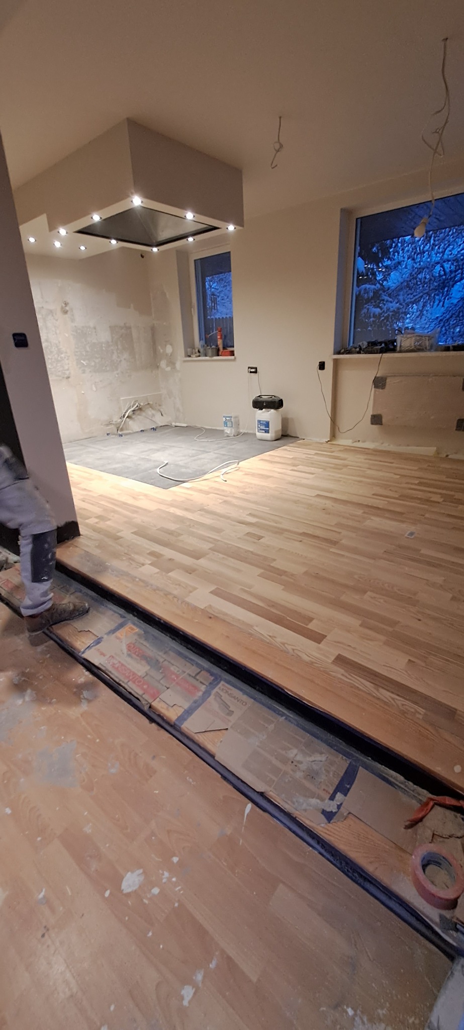Montaż drewnianego parkietu w trakcie remontu mieszkania, widoczne narzędzia i materiały budowlane, częściowo wykończona podłoga, przygotowana do dalszych prac wykończeniowych.