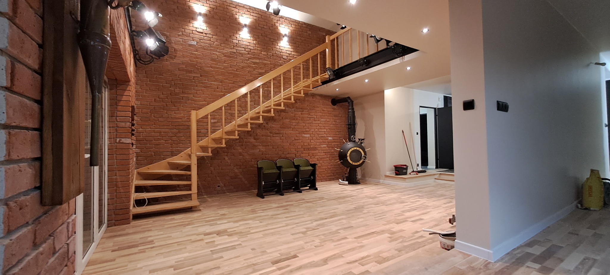 Przestronne wnętrze po remoncie z drewnianymi schodami, parkietem w jodełkę, ścianą z czerwonej cegły i designerskim piecem w stylu retro.