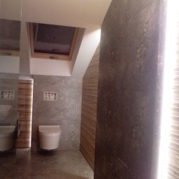 EKOMARBUD - Nowoczesna łazienka z betonowymi płytami ściennymi, podwieszaną toaletą i oknem dachowym, wykończona drewnianą boazerią, z widocznym fragmentem kabla na podłodze.