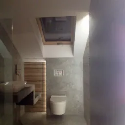 Nowoczesna łazienka z betonowymi ścianami, wiszącą toaletą, umywalką na betonowym blacie i oknem dachowym, widok z góry na niedokończone wykończenie.