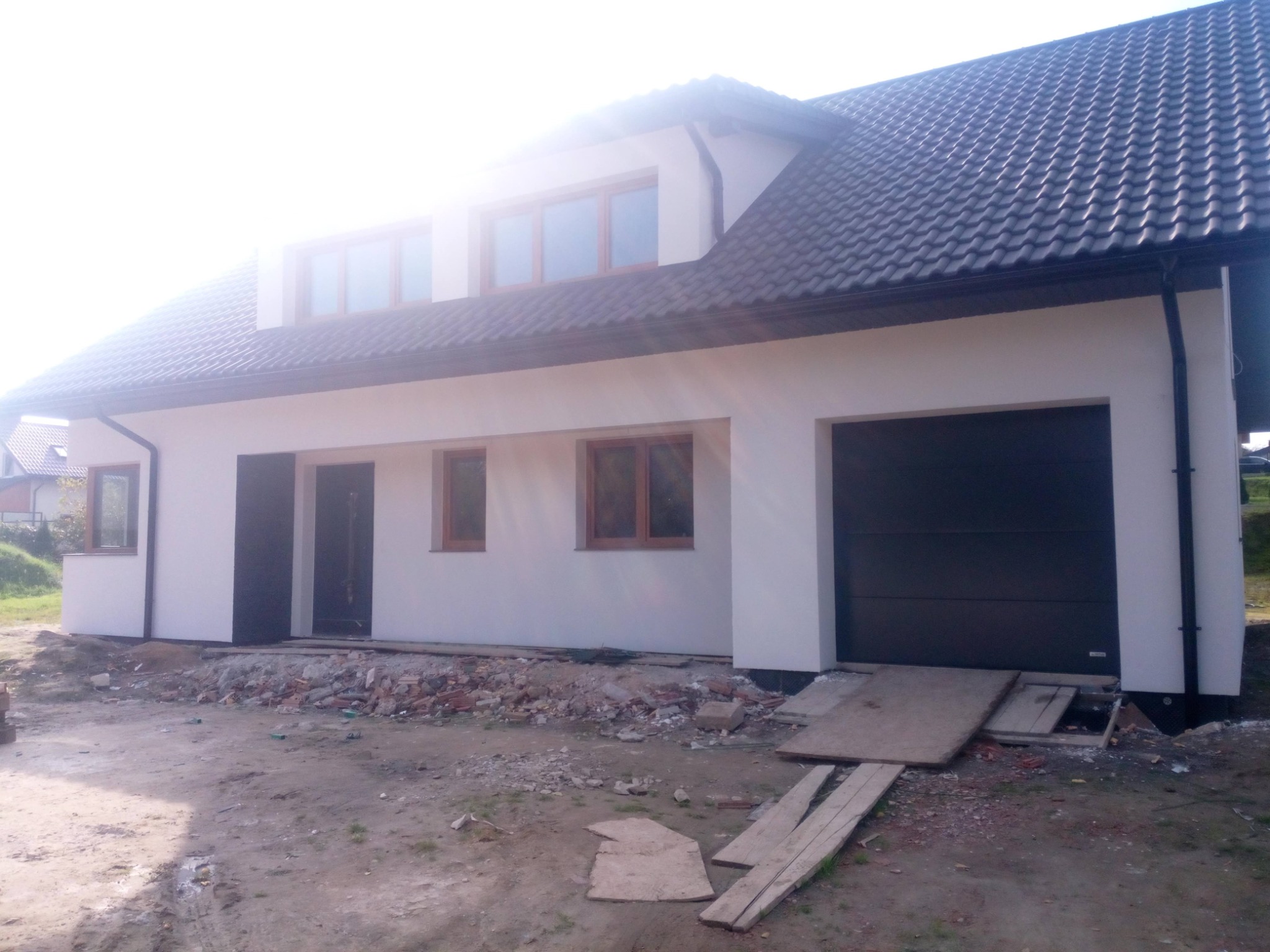 Nowo ocieplony dom jednorodzinny z grafitową stolarką okienną i garażem, widoczne resztki gruzu po pracach wykończeniowych.