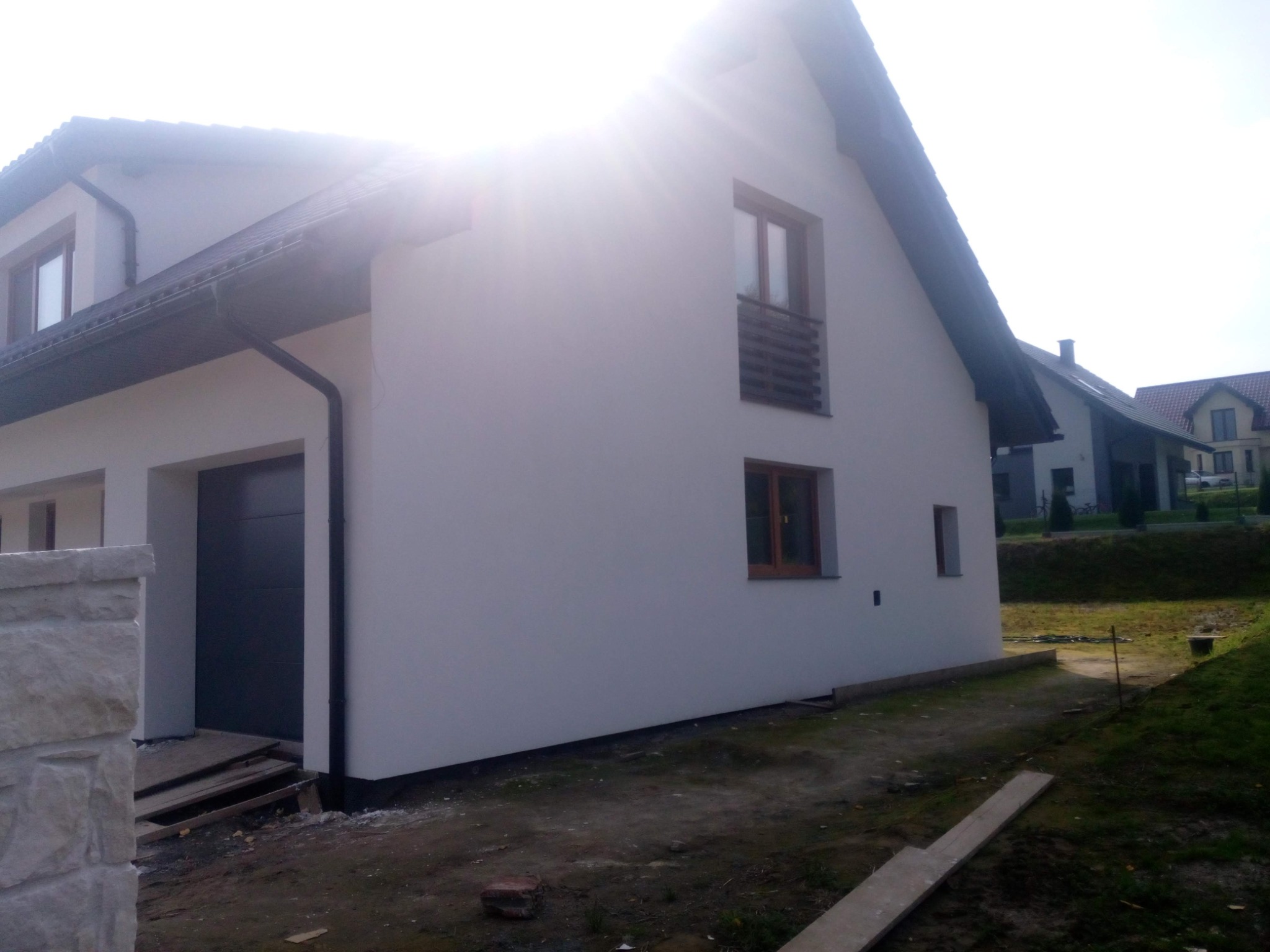 Ocieplony dom jednorodzinny z garażem i brązowymi ramami okiennymi, widok z boku w słoneczny dzień.