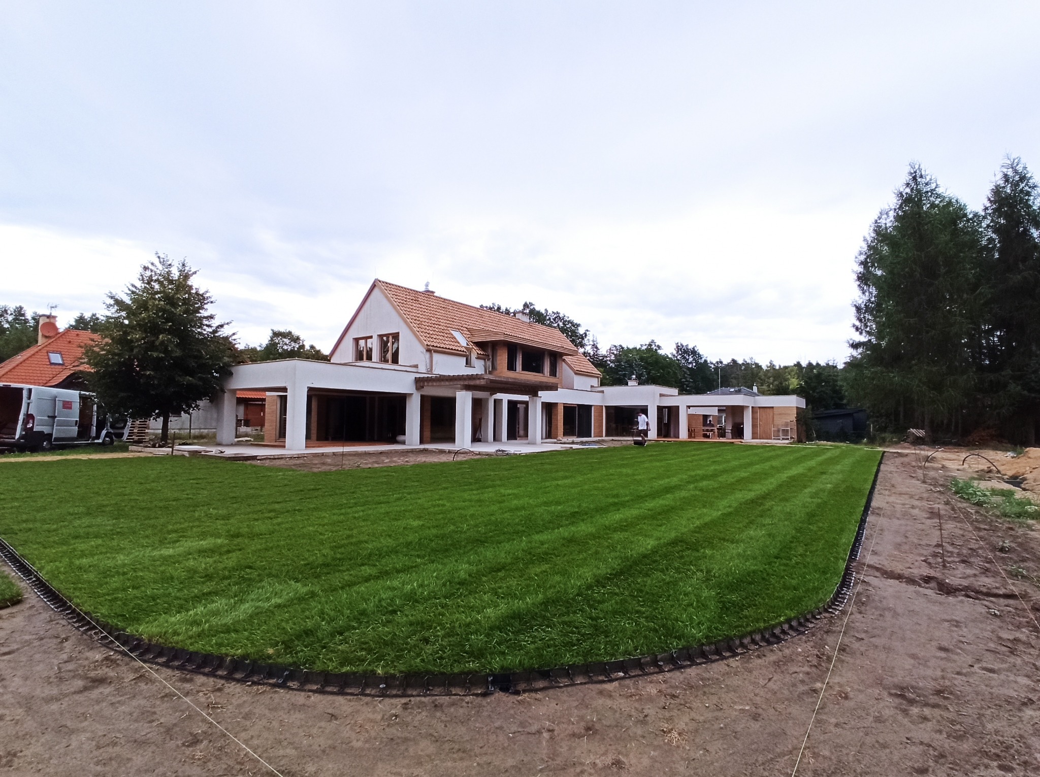 Rozległy trawnik z rolki przed nowoczesnym domem w trakcie budowy, widoczne obrzeża trawnika i przygotowany teren pod dalsze prace.