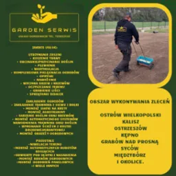 Mężczyzna w czarnej bluzie z logo firmy ogrodniczej rozsiewa nawóz lub nasiona z wózka na przygotowanym podłożu pod trawnik. W tle widoczne ogrodzenie i drzewa.