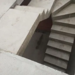 Surowe, spiralne schody z betonu w trakcie budowy, widoczne szare stopnie i fragment podłoża z ceglanym tłem, na powierzchni betonu widoczne niewielkie zabrudzenia.