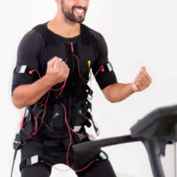 Uśmiechnięty mężczyzna w czarnym stroju do elektrostymulacji mięśni (EMS) z elektrodami i kablami, ćwiczący na bieżni.