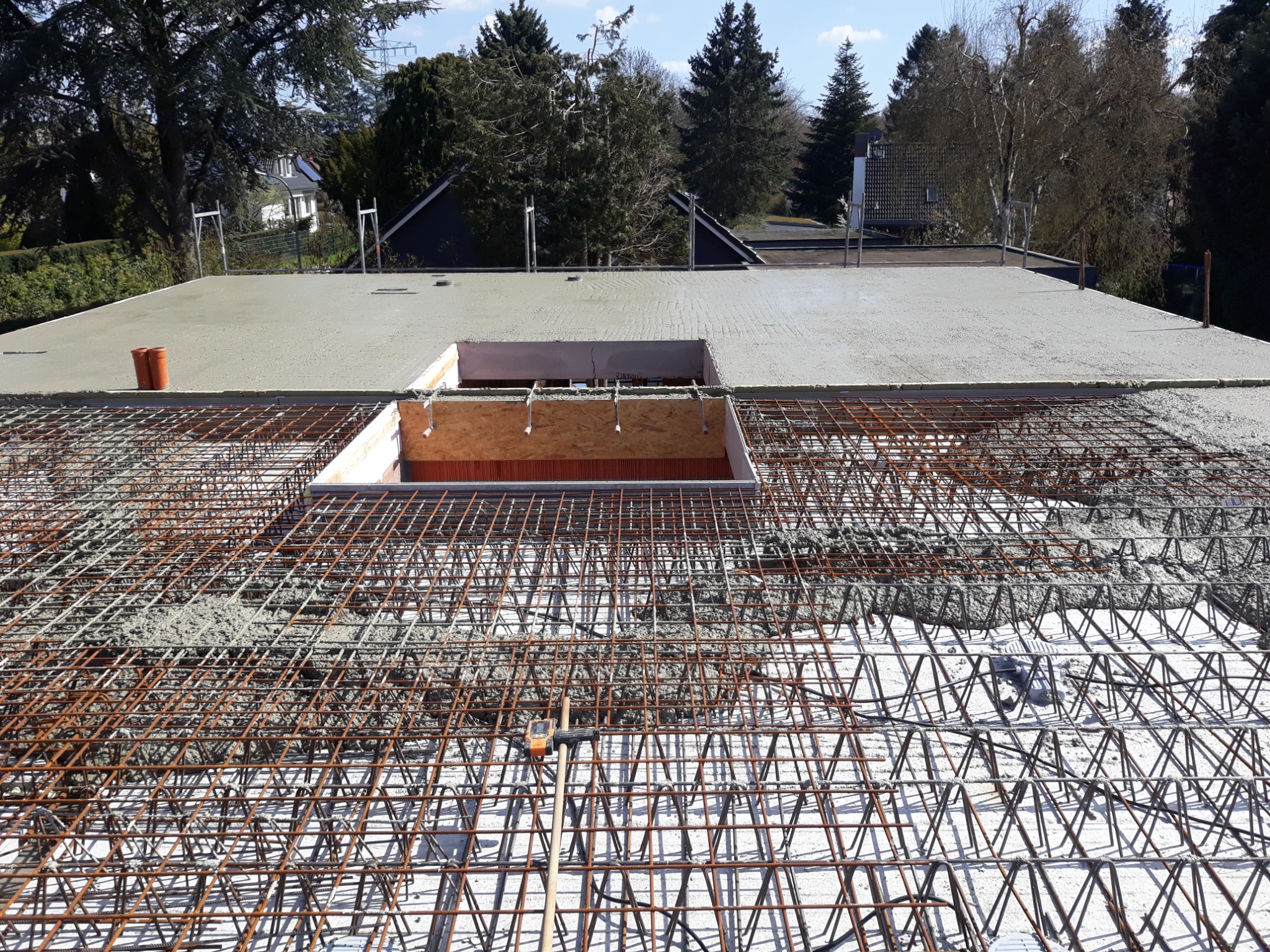 Zbrojenie stropu z wylewką betonu, widoczne deski szalunkowe otworu oraz narzędzie pomiarowe na siatce zbrojeniowej.