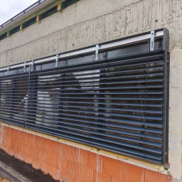 firmadavex.pl - Zewnętrzne żaluzje fasadowe w kolorze antracytowym zamontowane w budynku w trakcie budowy, widoczne surowe ściany z betonu i cegły.