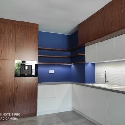 Glam House - Nowoczesna kuchnia z drewnianymi szafkami, białymi frontami i niebieską ścianą z półkami, oświetlona punktowo pod szafkami i półkami, z wbudowanym ekspresem do kawy.