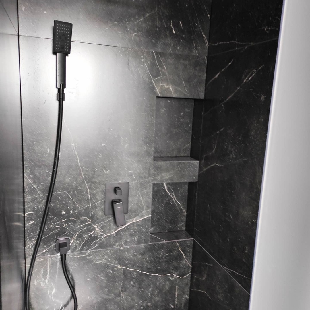Czarny, marmurkowy prysznic z wnękami na kosmetyki i minimalistyczną, kwadratową słuchawką oraz baterią w matowym wykończeniu.