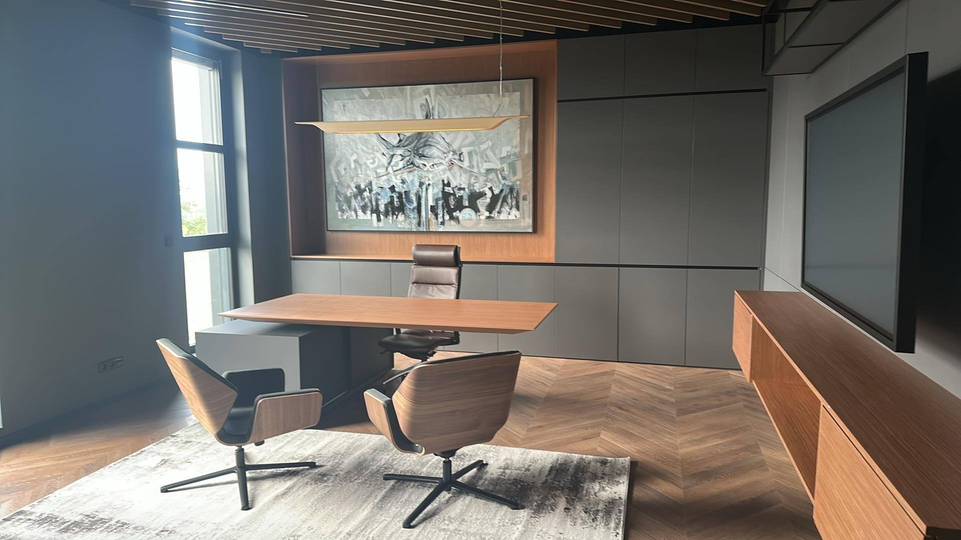 Nowoczesne wykończenie biura w Stróżach: drewniana podłoga w jodełkę, szare ściany, minimalistyczne meble i abstrakcyjny obraz nad biurkiem. Eleganckie i funkcjonalne.