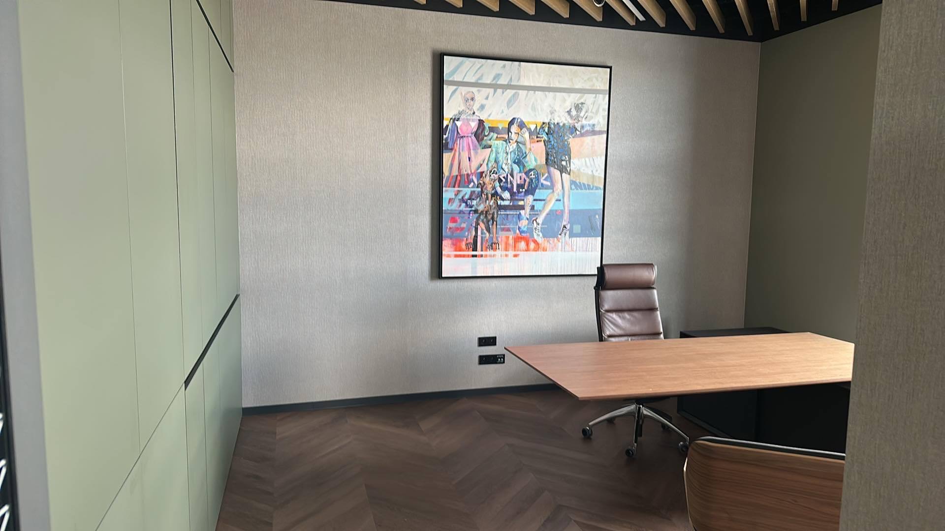 Nowoczesne biuro z parkietem w jodełkę, biurkiem, krzesłem i szafą w zabudowie. Na ścianie wisi obraz w czarnej ramie. Wykończenie wnętrza w stonowanych kolorach.