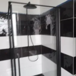 Nowoczesna kabina prysznicowa z czarną ramą i deszczownicą na tle ściany wyłożonej czarno-białymi, poziomymi pasami płytek.