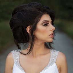 Karina Derda - Portret panny młodej w białej sukni z kryształkami, z upiętymi ciemnymi włosami i wyrazistym makijażem, profil na tle rozmytej zieleni.