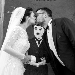 Karina Derda - Czarno-białe zdjęcie całującej się pary młodej na tle ściany z napisem 'Check Point Charlie' i wizerunkiem Charliego Chaplina.