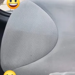 Częściowo wyczyszczone, jasnoszare siedzenie samochodowe z widoczną różnicą w kolorze i strukturze materiału, zarys odkurzacza w tle.