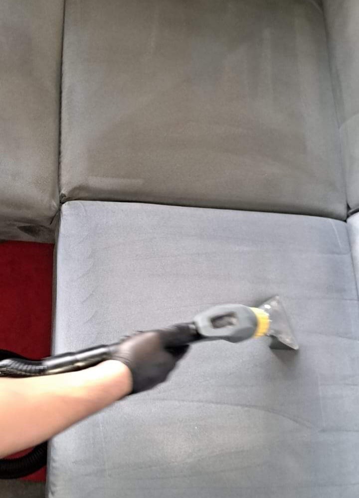 Czyszczenie szarej sofy parownicą; widoczna różnica w kolorze między wyczyszczoną a nieczyszczoną częścią tapicerki.