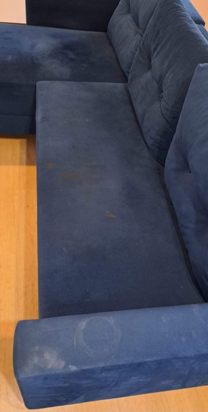 Fragment ciemnoniebieskiej, narożnej kanapy z widocznymi plamami i zabrudzeniami na siedzisku i boku, ukazujący potrzebę odświeżenia tapicerki.