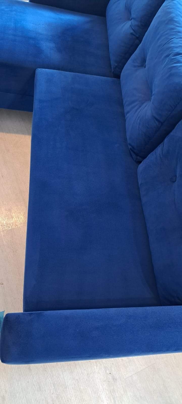 Fragment niebieskiej, welurowej sofy modułowej z poduchami, widoczny na jasnej podłodze.