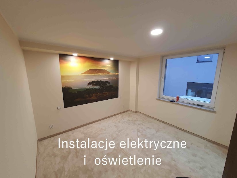 Wnętrze pokoju z nowym oświetleniem sufitowym typu downlight, widoczne puszki elektryczne na ścianie oraz fototapeta z motywem afrykańskiego krajobrazu z górą Kilimandżaro.