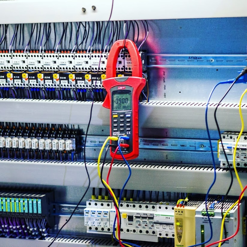 Panel elektryczny w Brzegu, podczas pomiarów prądu cęgowym miernikiem cyfrowym Uni-T UT243, widoczne liczne przewody i zabezpieczenia.