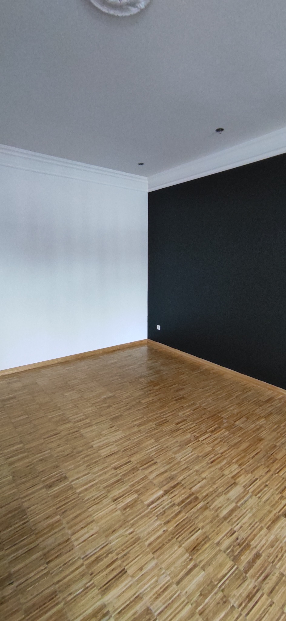 Pomalowane na biało i czarno ściany w pustym pokoju z parkietem ułożonym w jodełkę.