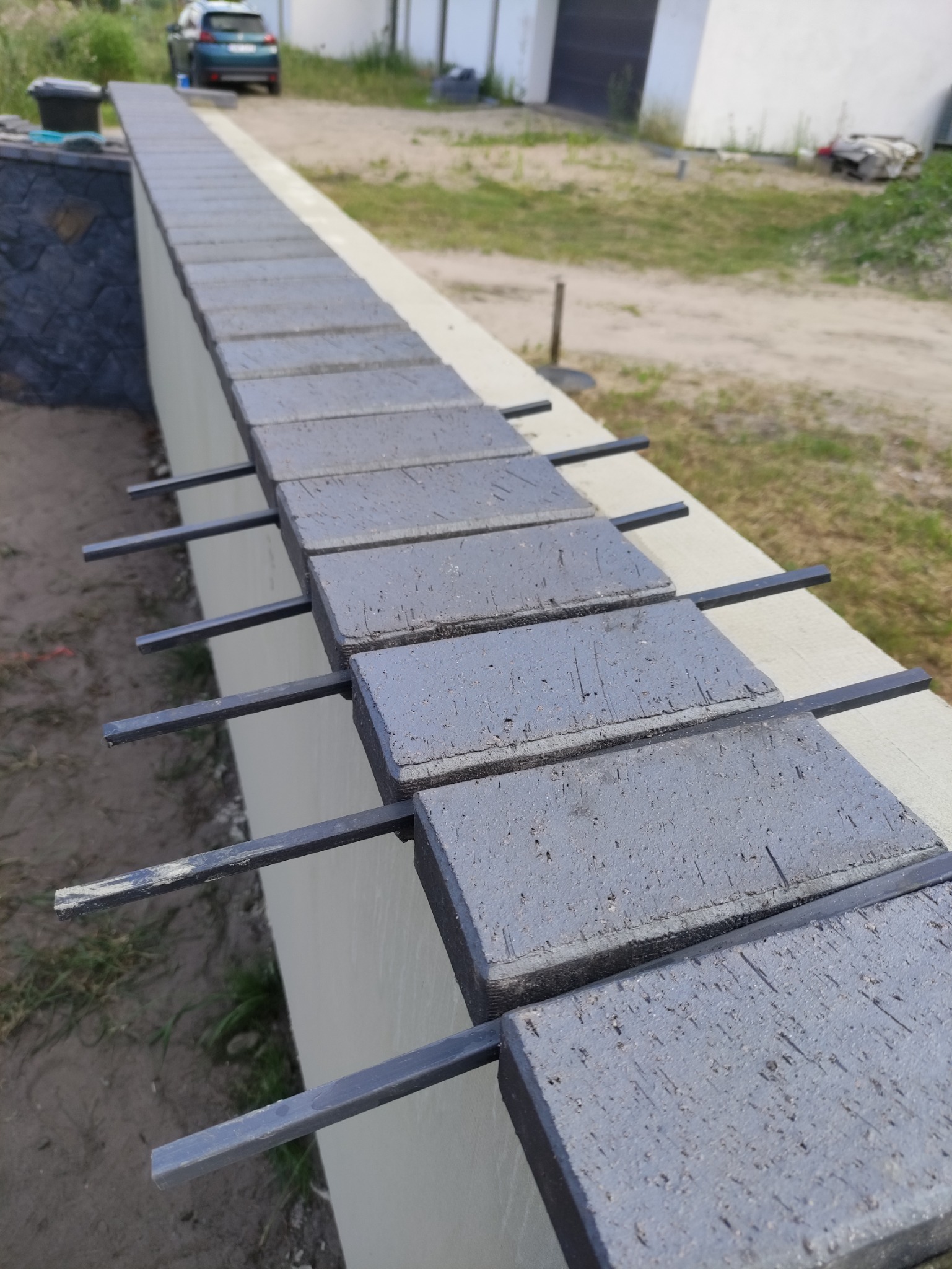 Montaż klinkieru na elewacji, widoczne metalowe wsporniki mocujące płytki, w tle trawnik i budynek.